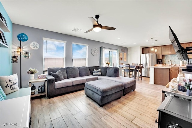 living room with light wood-style floors, visible vents, and a ceiling fan