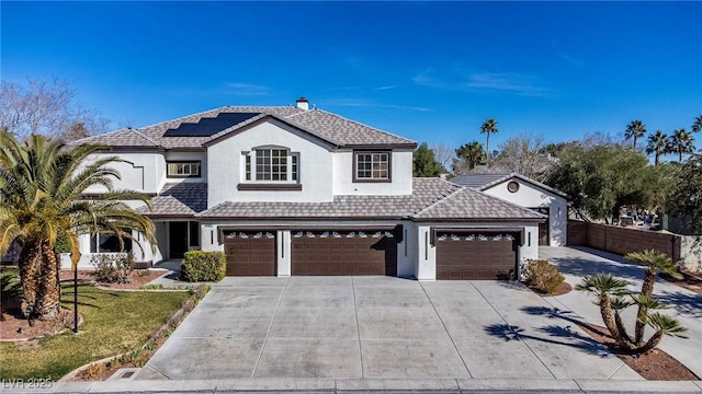 view of front of house with solar panels, fence, a tile roof, concrete driveway, and stucco siding