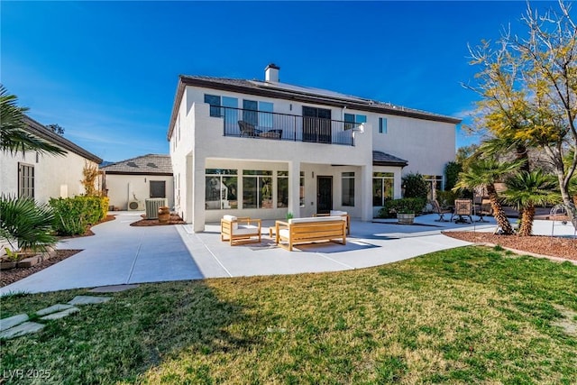 back of property featuring a balcony, central AC, a lawn, roof mounted solar panels, and a patio area