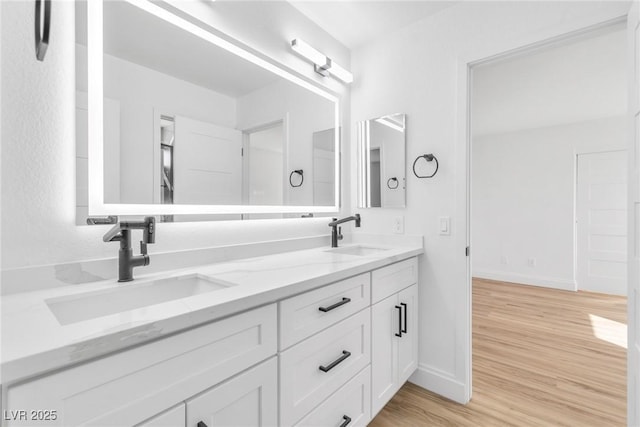 full bath with double vanity, a sink, baseboards, and wood finished floors