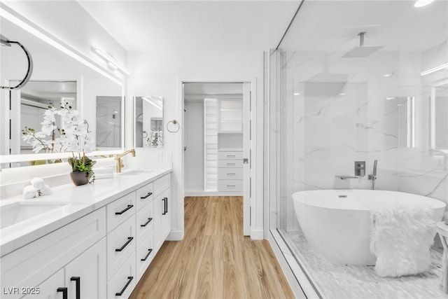 bathroom featuring double vanity, wood finished floors, a sink, and a marble finish shower