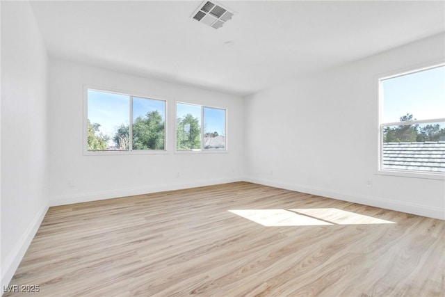 spare room featuring light wood-type flooring, visible vents, and plenty of natural light