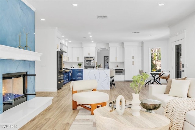 living room featuring arched walkways, light wood-style flooring, recessed lighting, visible vents, and a high end fireplace