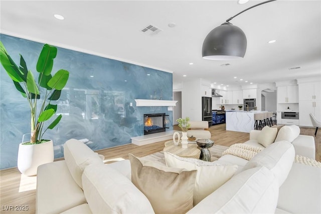 living area with light wood-style floors, recessed lighting, visible vents, and a fireplace