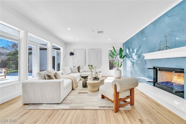 living room featuring recessed lighting, visible vents, wood finished floors, a warm lit fireplace, and baseboards