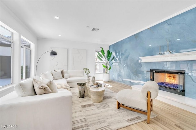 living room with a fireplace, recessed lighting, visible vents, ornamental molding, and wood finished floors