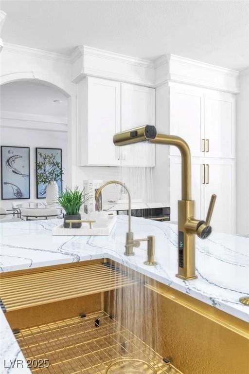 room details with arched walkways, ornamental molding, light stone countertops, and white cabinets