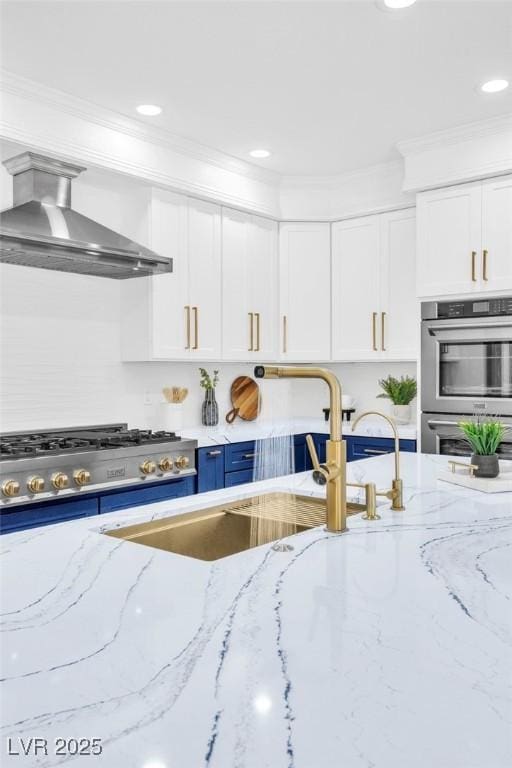 kitchen featuring double oven, white cabinets, ornamental molding, and wall chimney range hood