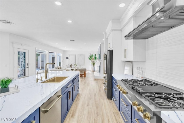 kitchen with wall chimney exhaust hood, appliances with stainless steel finishes, blue cabinets, white cabinetry, and a sink