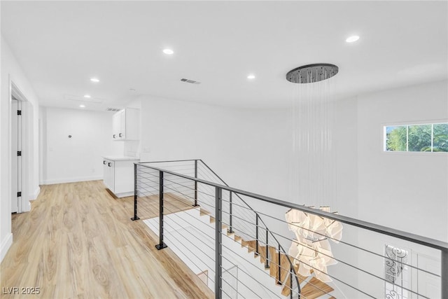 corridor with light wood finished floors, visible vents, baseboards, an upstairs landing, and recessed lighting