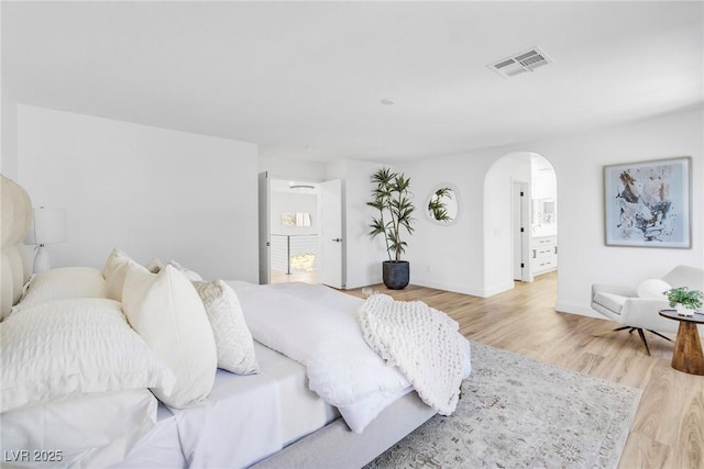 bedroom featuring light wood-style flooring, visible vents, arched walkways, and baseboards