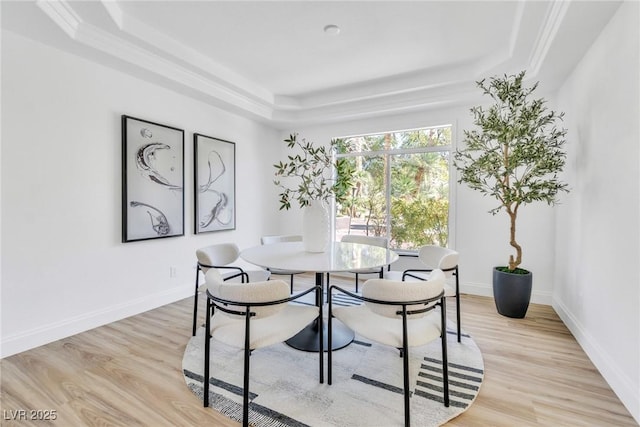 dining space featuring a raised ceiling, light wood-style flooring, and baseboards