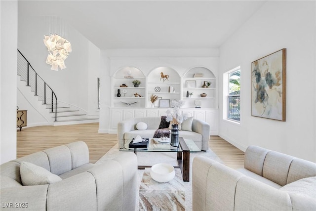 living room featuring built in shelves, wood finished floors, baseboards, and stairs