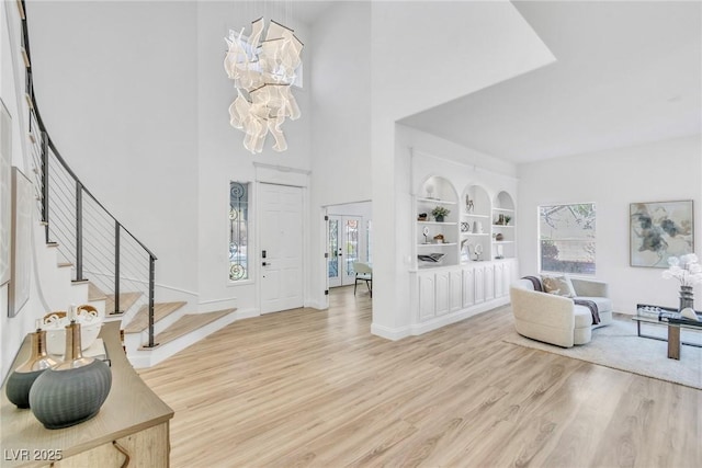 foyer featuring light wood-style floors, a chandelier, baseboards, and stairs