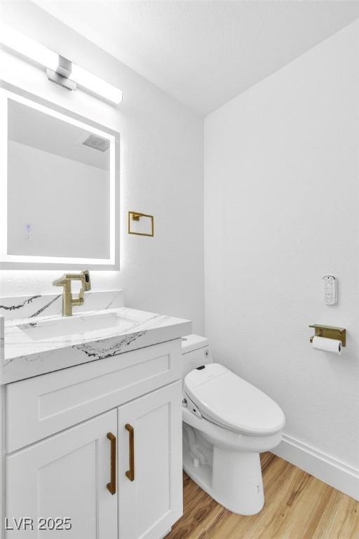 bathroom featuring toilet, baseboards, wood finished floors, and vanity