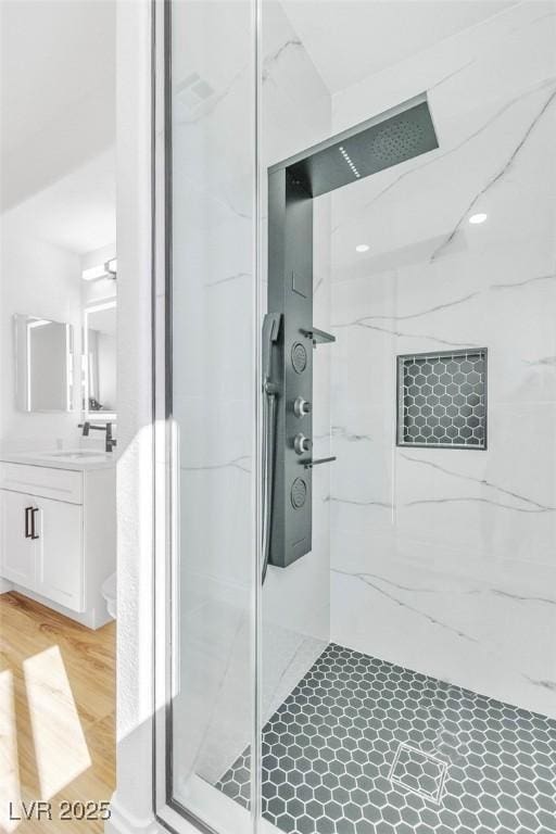 full bathroom with a marble finish shower, wood finished floors, and vanity