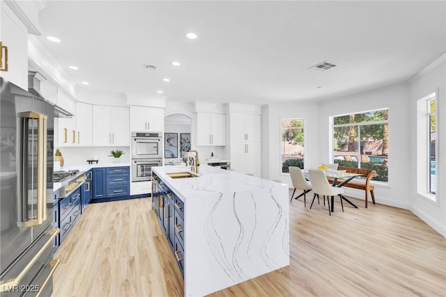 kitchen with blue cabinetry, stainless steel appliances, visible vents, white cabinets, and a sink