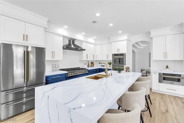 kitchen featuring visible vents, wall chimney exhaust hood, stainless steel appliances, blue cabinetry, and a sink