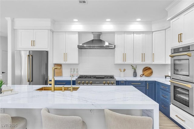 kitchen with blue cabinetry, stainless steel appliances, a kitchen bar, a sink, and wall chimney exhaust hood