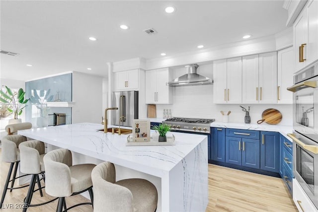 kitchen with visible vents, white cabinets, high end appliances, wall chimney exhaust hood, and blue cabinetry