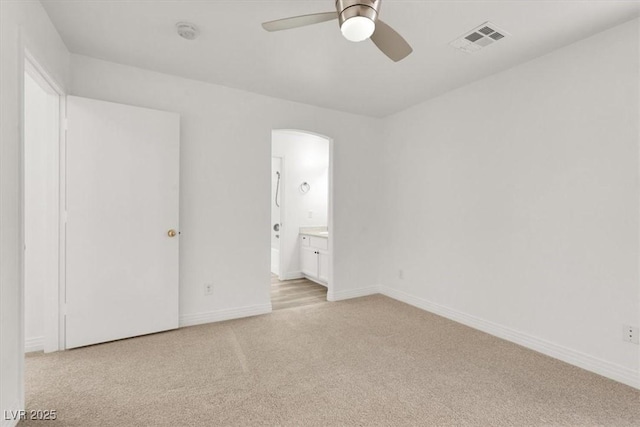 unfurnished bedroom featuring baseboards, visible vents, arched walkways, and light colored carpet