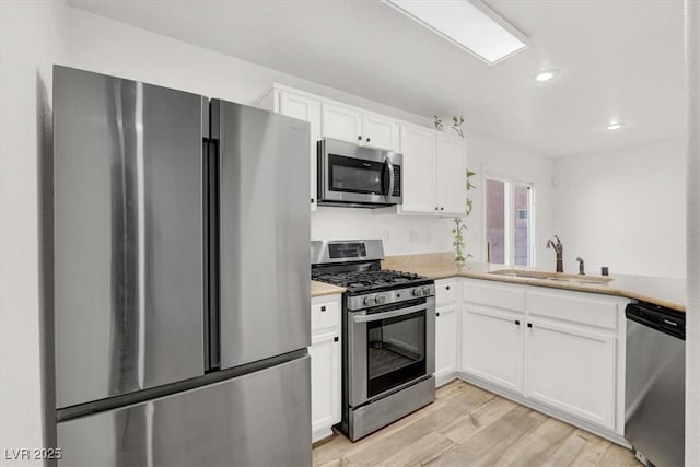 kitchen with light countertops, appliances with stainless steel finishes, a sink, and white cabinets