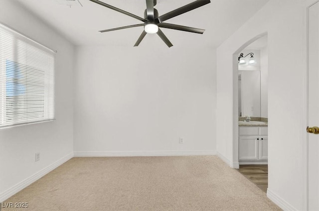 spare room with light carpet, ceiling fan, baseboards, and arched walkways