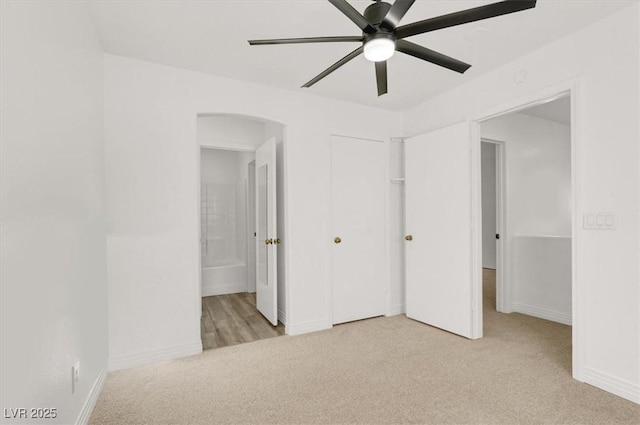 unfurnished bedroom with light carpet, baseboards, arched walkways, ensuite bathroom, and a closet