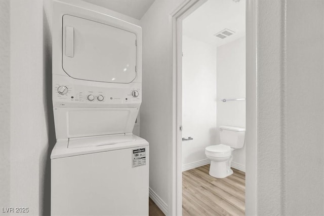 clothes washing area featuring light wood-style flooring, laundry area, visible vents, baseboards, and stacked washing maching and dryer