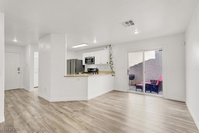 kitchen featuring visible vents, a peninsula, stainless steel appliances, light wood-type flooring, and white cabinetry