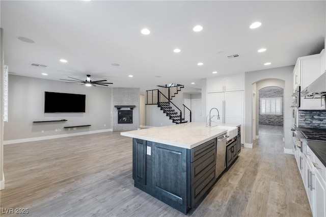 kitchen with a large fireplace, a center island with sink, visible vents, arched walkways, and white cabinets