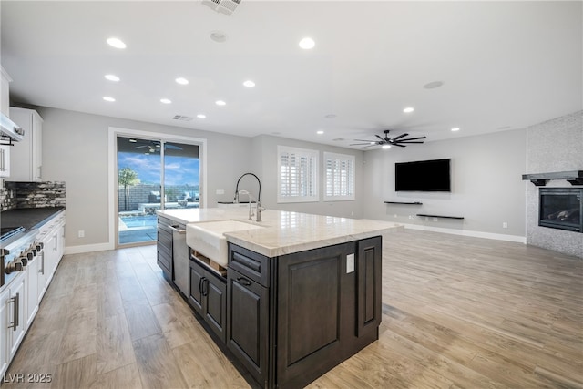 kitchen with a large fireplace, light wood-type flooring, a sink, and white cabinets