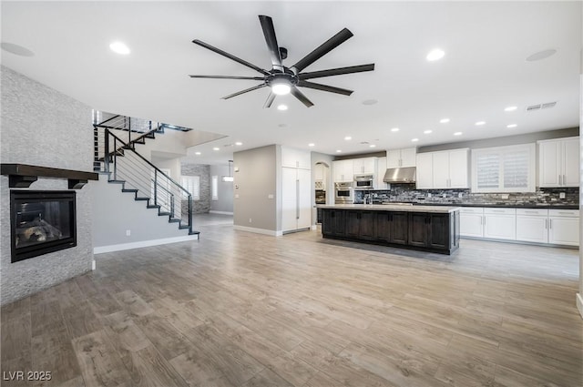 unfurnished living room featuring recessed lighting, visible vents, stairway, light wood-style floors, and a glass covered fireplace