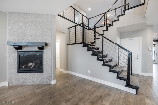 staircase featuring a high ceiling, baseboards, a fireplace, and wood finished floors