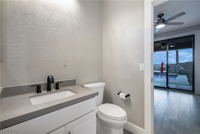 bathroom with ceiling fan, a textured wall, toilet, wood finished floors, and vanity