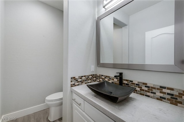 bathroom with toilet, wood finished floors, vanity, baseboards, and decorative backsplash