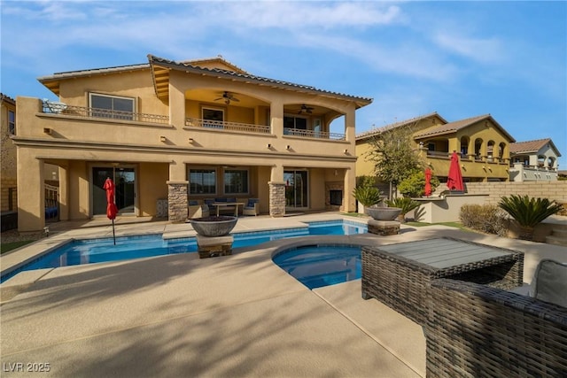 back of property featuring a balcony, ceiling fan, an in ground hot tub, a patio area, and stucco siding