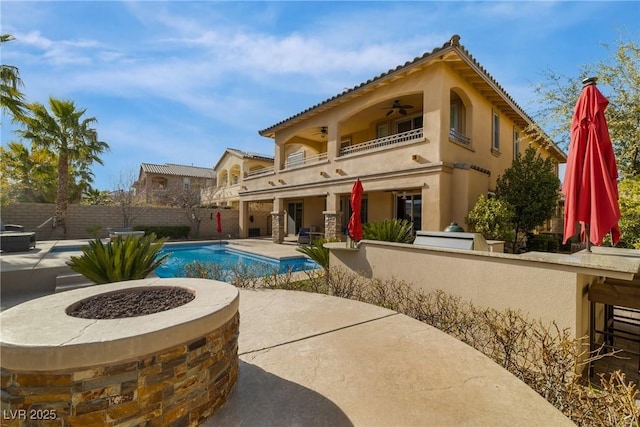 back of property featuring a fenced in pool, a patio area, fence, a balcony, and ceiling fan