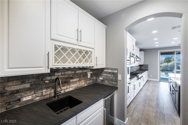 kitchen with visible vents, arched walkways, dark countertops, a sink, and backsplash