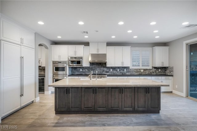 kitchen with arched walkways, stainless steel double oven, visible vents, and under cabinet range hood