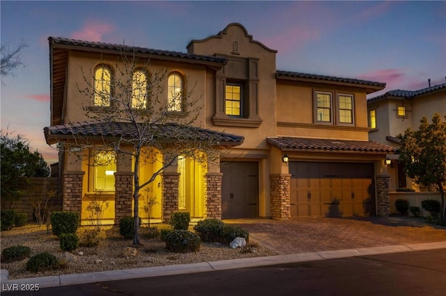 mediterranean / spanish-style house with decorative driveway, stucco siding, a garage, stone siding, and a tiled roof