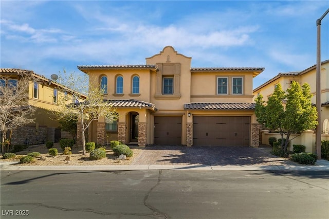 mediterranean / spanish home with a garage, a tiled roof, decorative driveway, and stucco siding