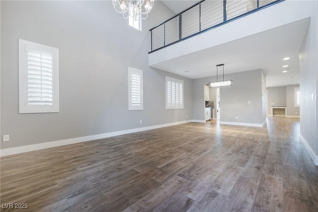 unfurnished living room featuring baseboards, a high ceiling, a chandelier, and wood finished floors