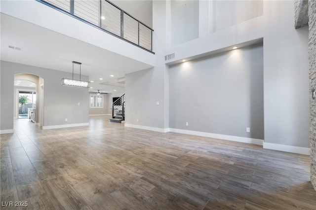 unfurnished living room featuring visible vents, arched walkways, and wood finished floors