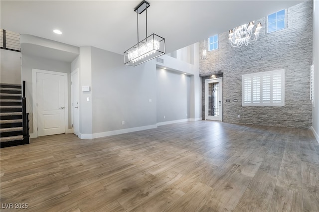 unfurnished living room featuring a towering ceiling, stairway, wood finished floors, a chandelier, and baseboards