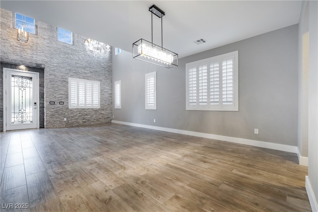 interior space featuring visible vents, a towering ceiling, an inviting chandelier, wood finished floors, and baseboards