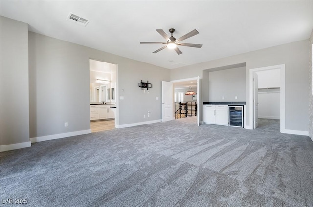 unfurnished living room featuring beverage cooler, visible vents, baseboards, a ceiling fan, and carpet floors