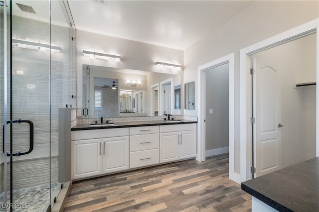 full bath with double vanity, wood finished floors, a sink, and a shower stall