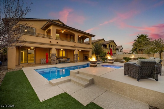 back of property featuring an outdoor fire pit, a balcony, fence, a fenced in pool, and a patio area