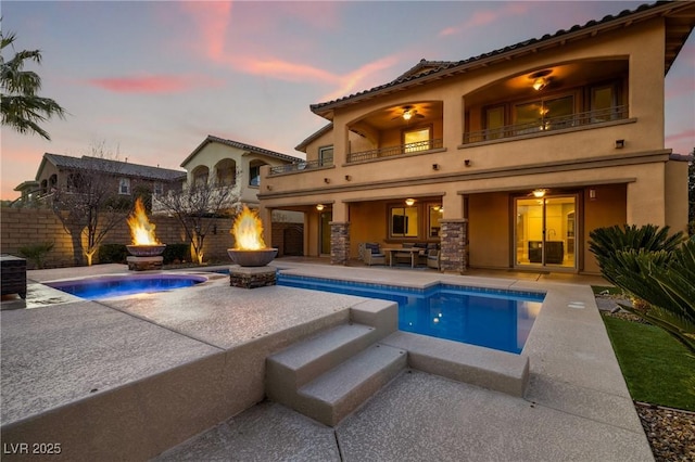 rear view of house with a balcony, a fire pit, a fenced in pool, stucco siding, and a patio area